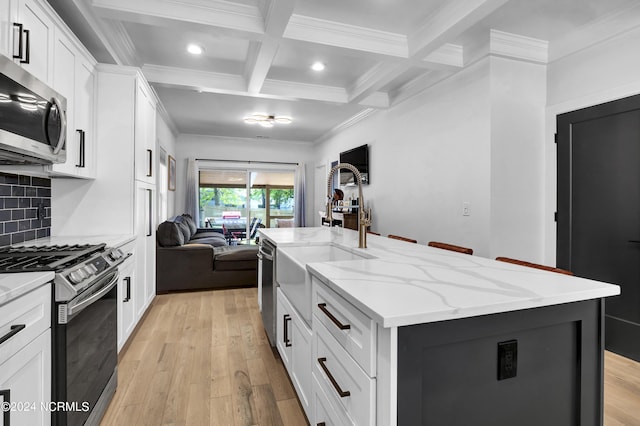 kitchen with appliances with stainless steel finishes, beamed ceiling, light stone countertops, a kitchen island with sink, and white cabinets