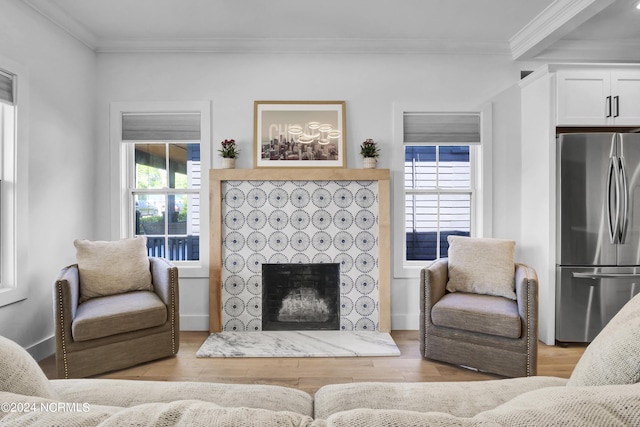 living room featuring crown molding, a tiled fireplace, and light wood-type flooring