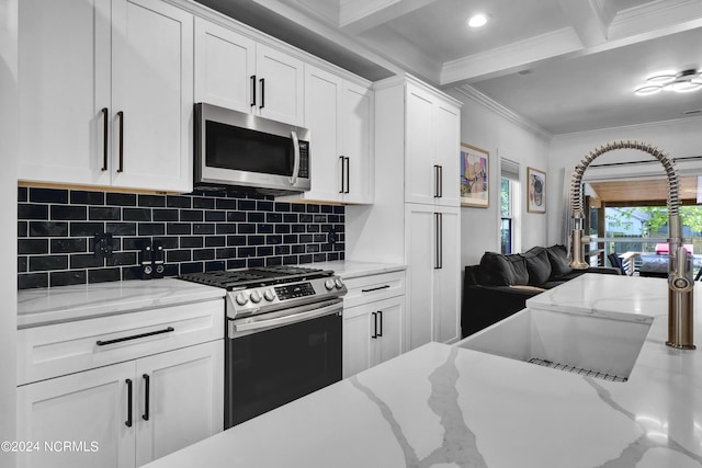 kitchen with appliances with stainless steel finishes, light stone counters, ornamental molding, white cabinets, and beamed ceiling