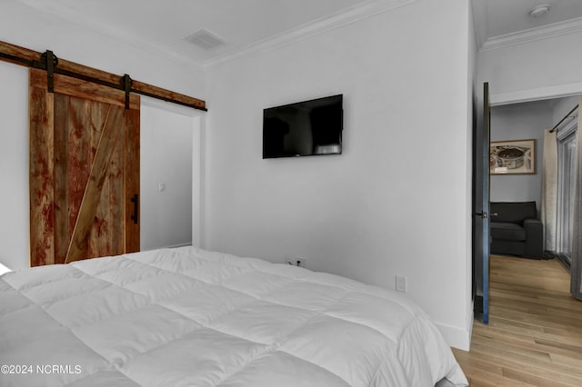 bedroom with ornamental molding, a barn door, and light wood-type flooring