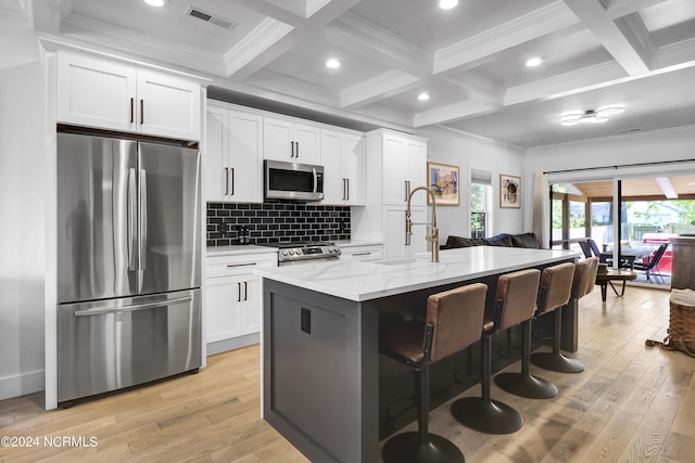 kitchen with appliances with stainless steel finishes, white cabinetry, a kitchen breakfast bar, light stone countertops, and a center island with sink