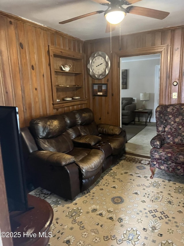 living room featuring built in shelves, ceiling fan, and wood walls