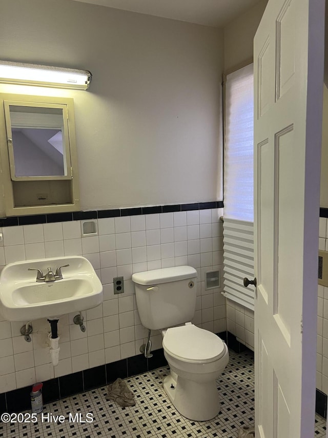 bathroom with toilet, tile patterned flooring, sink, and tile walls