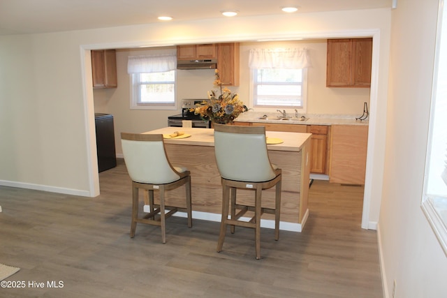 kitchen featuring stainless steel electric range oven, light countertops, light wood-type flooring, a breakfast bar, and under cabinet range hood