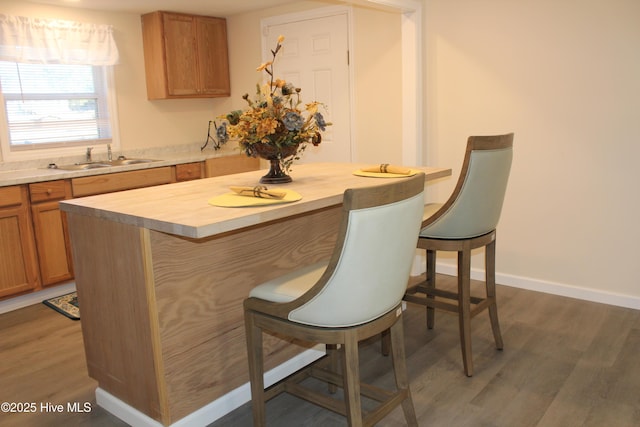 kitchen featuring light wood-type flooring, a breakfast bar, a center island, brown cabinets, and baseboards