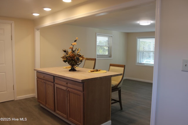 kitchen with brown cabinetry, a breakfast bar area, dark wood finished floors, and baseboards
