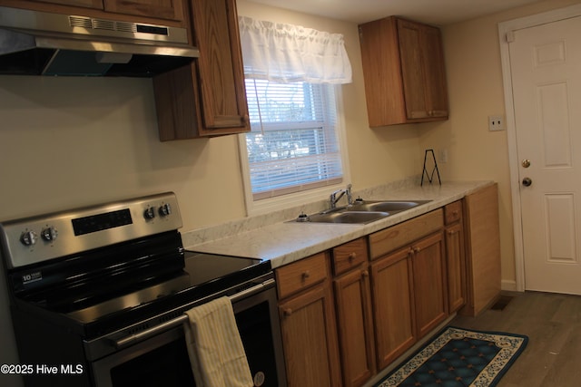 kitchen with a sink, dark wood-style flooring, electric stove, under cabinet range hood, and brown cabinetry