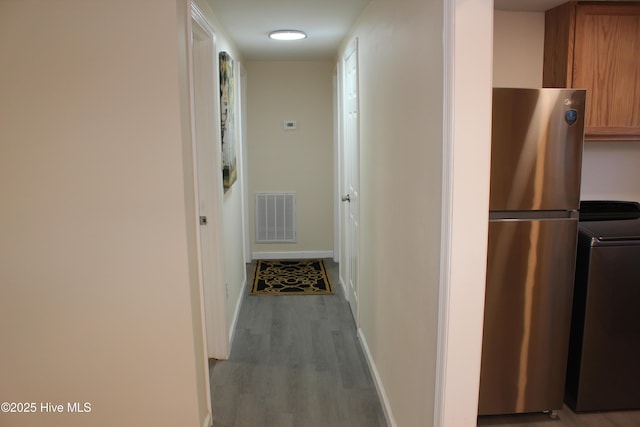 corridor with washer / clothes dryer, wood finished floors, baseboards, and visible vents