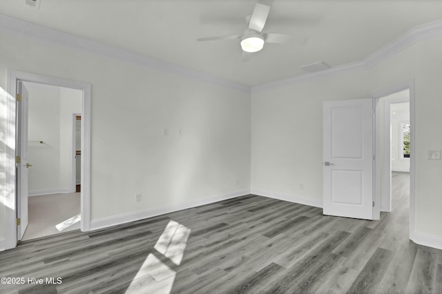 empty room featuring baseboards, attic access, wood finished floors, and crown molding