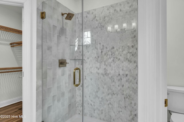 bathroom featuring a stall shower, toilet, a walk in closet, and wood finished floors