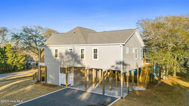 back of house featuring a patio, stairway, gravel driveway, a shingled roof, and a carport