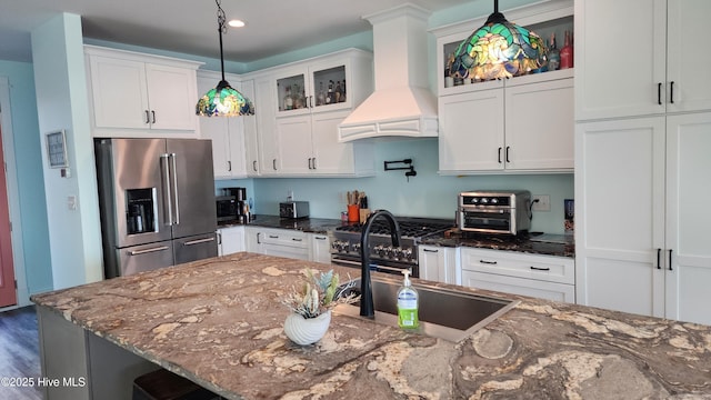 kitchen with high quality appliances, premium range hood, white cabinetry, and dark stone counters