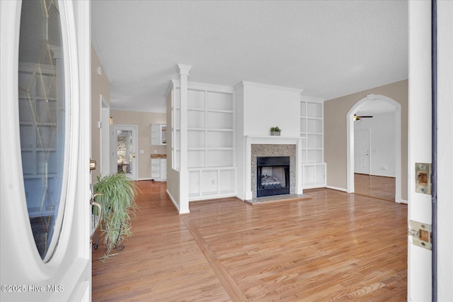 unfurnished living room with built in features, light hardwood / wood-style flooring, ornamental molding, and a textured ceiling