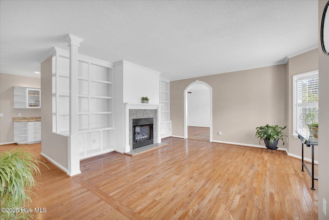 unfurnished living room with built in shelves, light hardwood / wood-style flooring, ornamental molding, and a textured ceiling