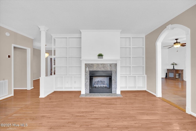 unfurnished living room with built in shelves, a textured ceiling, light wood-type flooring, ornamental molding, and a fireplace