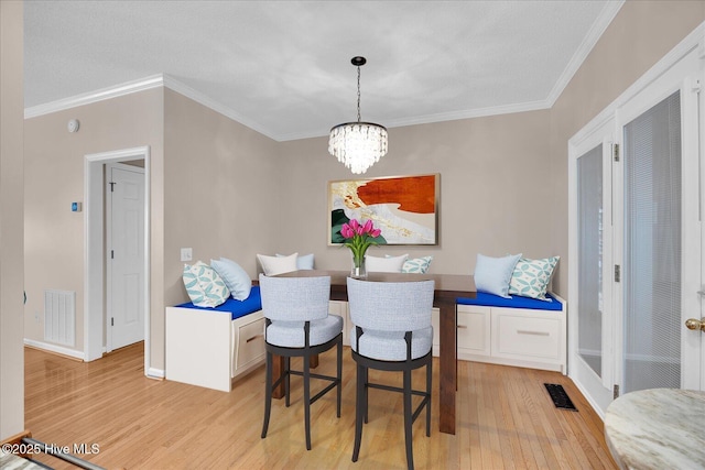 dining space featuring crown molding, an inviting chandelier, and light wood-type flooring