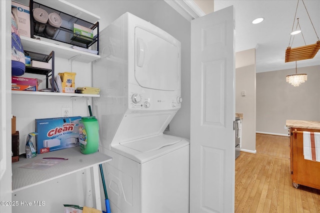 laundry room with a notable chandelier, stacked washer / dryer, and light wood-type flooring