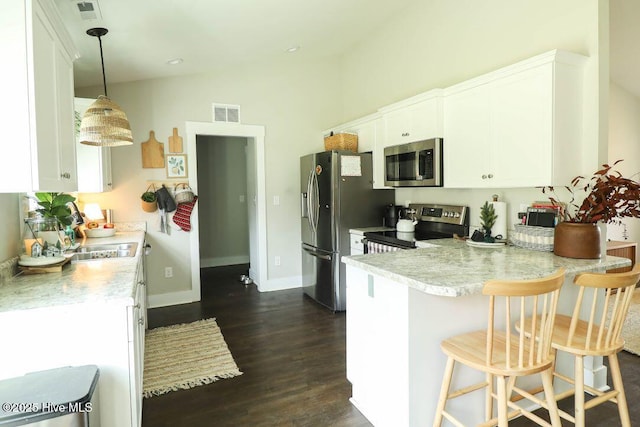 kitchen with a kitchen bar, white cabinetry, hanging light fixtures, appliances with stainless steel finishes, and kitchen peninsula