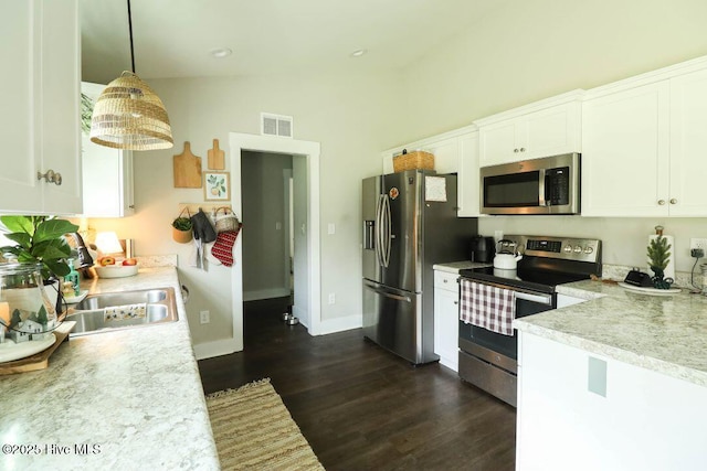 kitchen featuring white cabinetry, decorative light fixtures, vaulted ceiling, appliances with stainless steel finishes, and dark hardwood / wood-style flooring