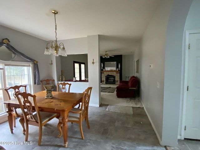 dining area featuring a fireplace and ceiling fan with notable chandelier