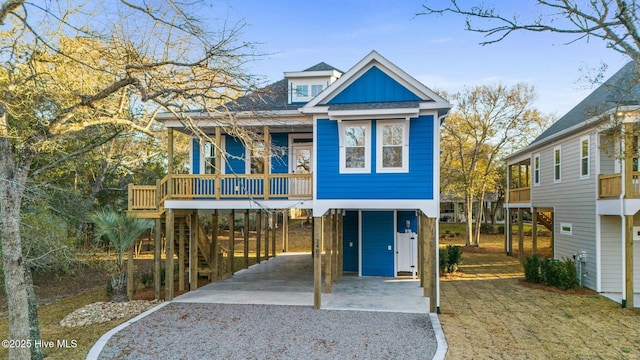 beach home featuring driveway, a porch, board and batten siding, a shingled roof, and a carport