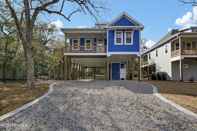 raised beach house featuring gravel driveway, a carport, stairs, and board and batten siding