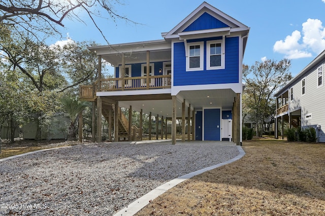 coastal home with board and batten siding, a carport, gravel driveway, and stairs