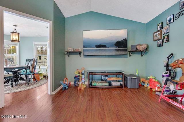 game room featuring lofted ceiling, hardwood / wood-style flooring, and a textured ceiling