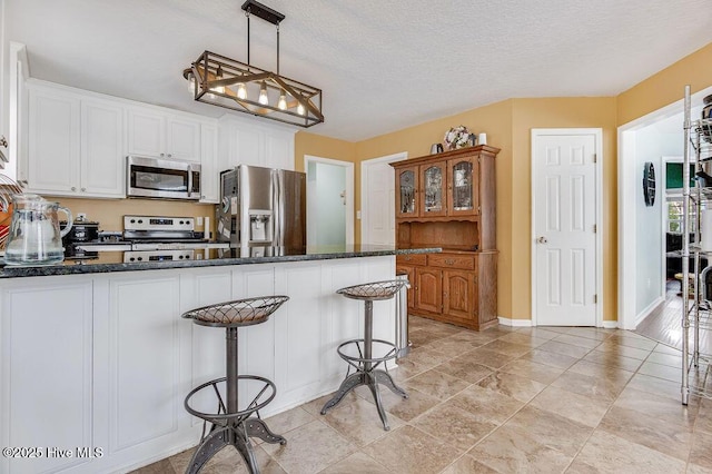 kitchen with decorative light fixtures, white cabinets, a kitchen bar, stainless steel appliances, and a textured ceiling