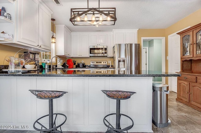 kitchen with appliances with stainless steel finishes, white cabinetry, a breakfast bar area, hanging light fixtures, and kitchen peninsula