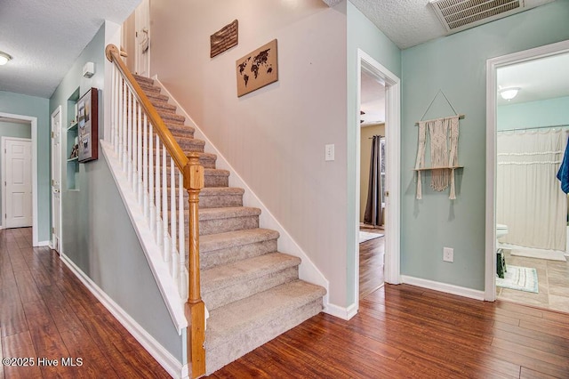 stairway with wood-type flooring and a textured ceiling