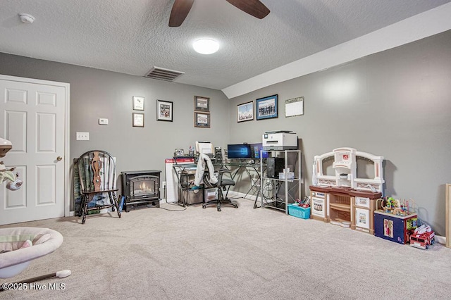 carpeted home office featuring a textured ceiling, ceiling fan, and a wood stove