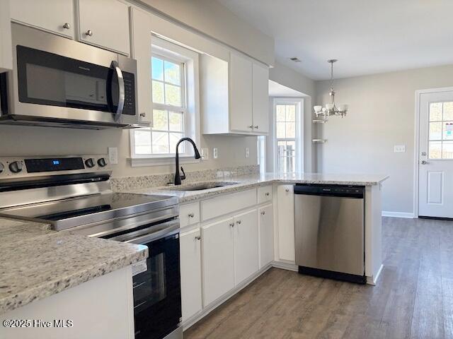 kitchen featuring pendant lighting, sink, appliances with stainless steel finishes, white cabinetry, and kitchen peninsula