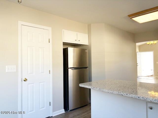 kitchen featuring dark wood-type flooring, stainless steel refrigerator, white cabinetry, light stone counters, and a notable chandelier