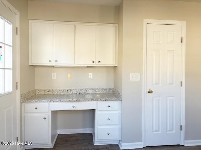 unfurnished office with a wealth of natural light, built in desk, and dark wood-type flooring