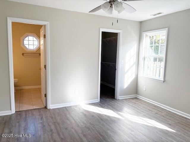 unfurnished bedroom with a walk in closet, ensuite bath, a closet, hardwood / wood-style flooring, and ceiling fan