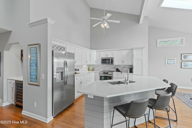 kitchen featuring sink, a breakfast bar area, white cabinets, stainless steel appliances, and a center island with sink