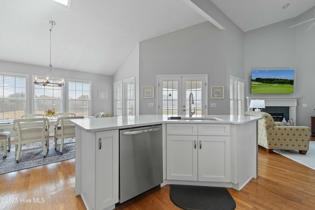 kitchen featuring sink, white cabinetry, hanging light fixtures, stainless steel dishwasher, and light hardwood / wood-style floors