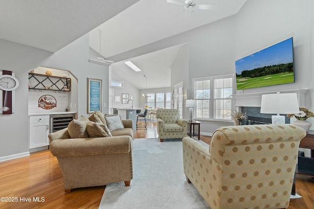 living room with ceiling fan, high vaulted ceiling, wine cooler, wet bar, and light wood-type flooring