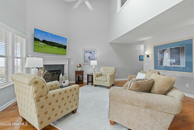 living room featuring ceiling fan, wood-type flooring, a high end fireplace, and a high ceiling