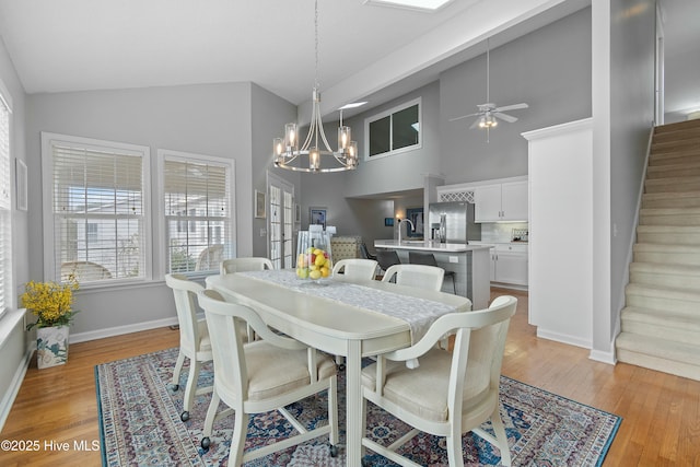 dining area featuring ceiling fan with notable chandelier, high vaulted ceiling, sink, and light hardwood / wood-style floors