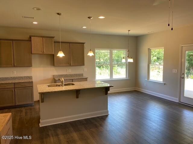kitchen featuring hanging light fixtures, light stone countertops, dark wood-style flooring, and a sink