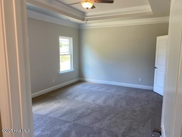 unfurnished room featuring a ceiling fan, a tray ceiling, dark carpet, baseboards, and ornamental molding
