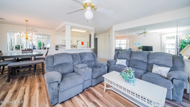 living room with ceiling fan with notable chandelier, decorative columns, and light wood-type flooring