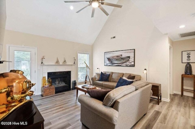 living room with plenty of natural light, high vaulted ceiling, a premium fireplace, and light wood-type flooring