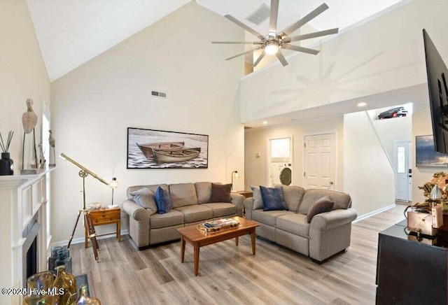 living room featuring washer / dryer, high vaulted ceiling, ceiling fan, and light wood-type flooring