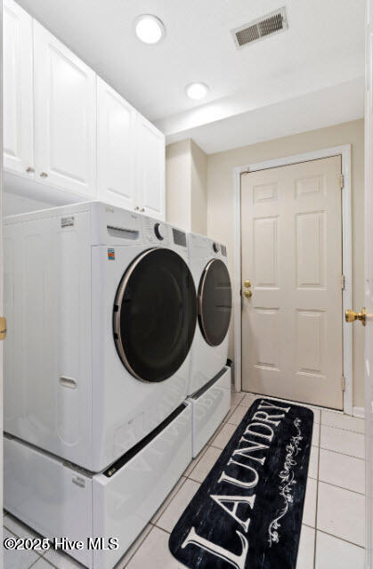 washroom featuring cabinets, washing machine and clothes dryer, and light tile patterned flooring