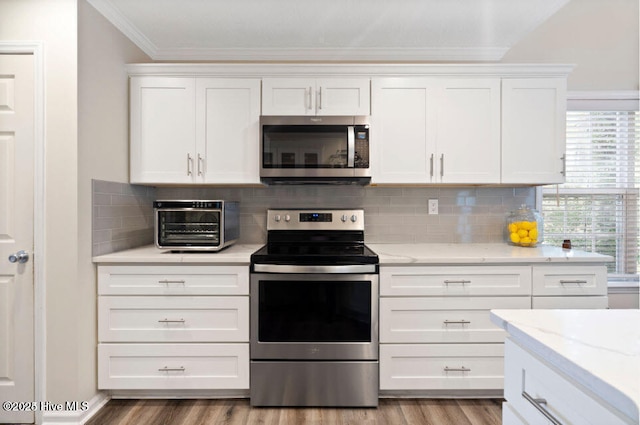 kitchen with white cabinetry, tasteful backsplash, light stone counters, ornamental molding, and stainless steel appliances