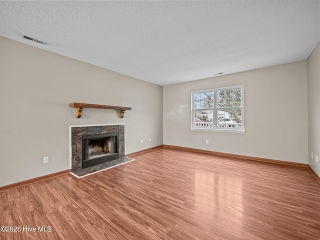 unfurnished living room with a high end fireplace, light hardwood / wood-style floors, and a textured ceiling