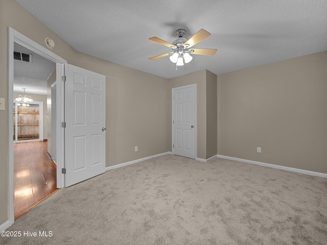 unfurnished bedroom featuring ceiling fan with notable chandelier, light carpet, and a textured ceiling